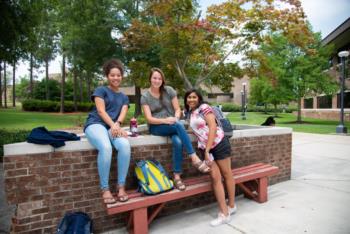 three students sitting on a bench outdoors