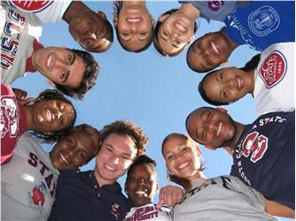 group of students in a circle looking down at camera