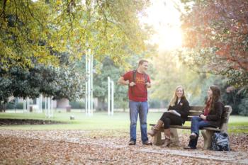 students chatting on campus bench in fall